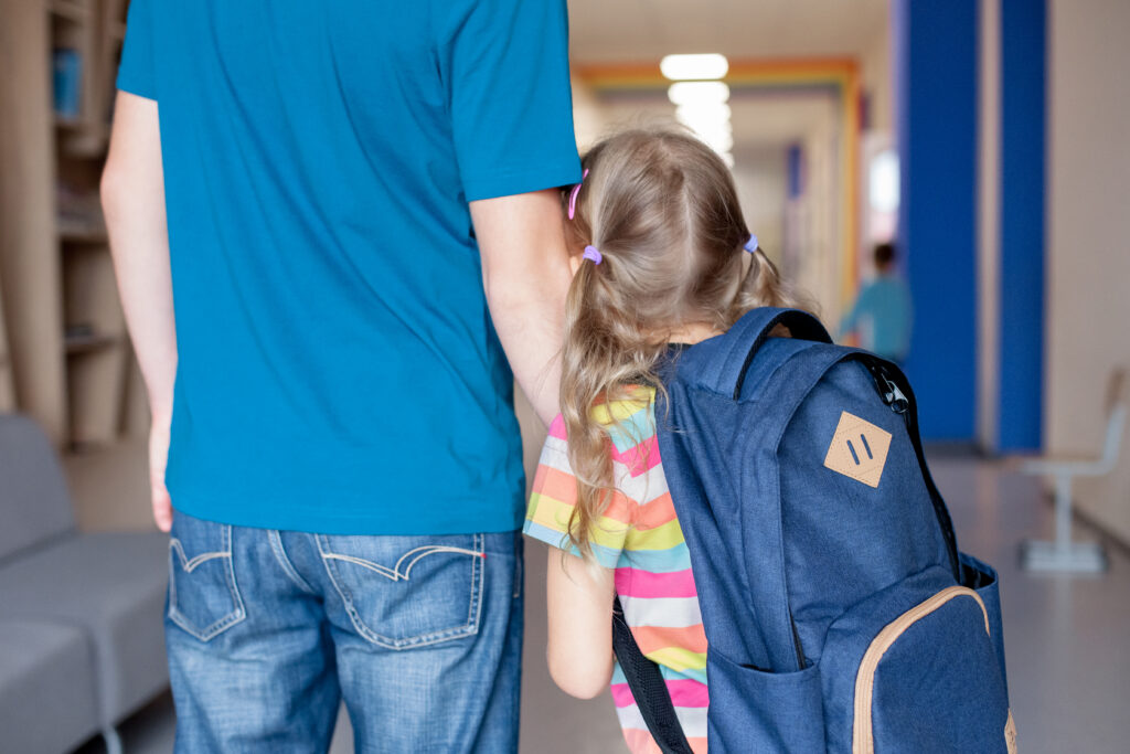 Daughter with backpack on clinging to father at school doors