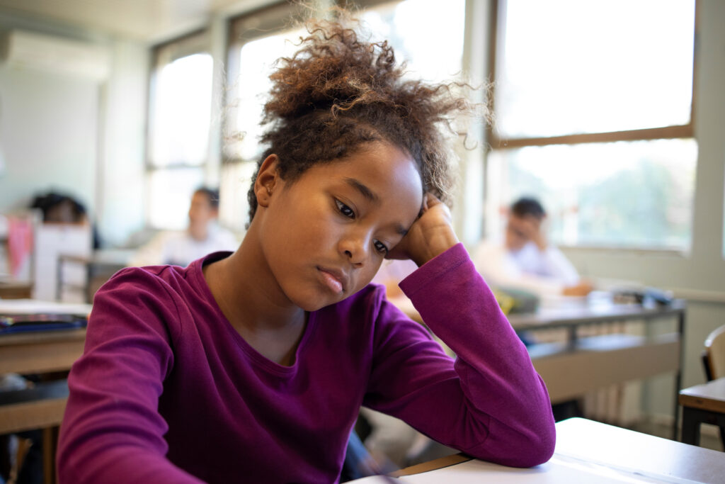 Sad schoolgirl sulking at desk in classroom