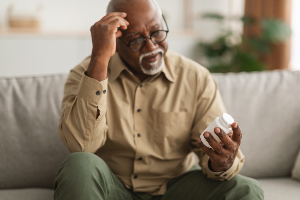 Senior African American Man Holding Medical Pills Reading Instruction Indoor